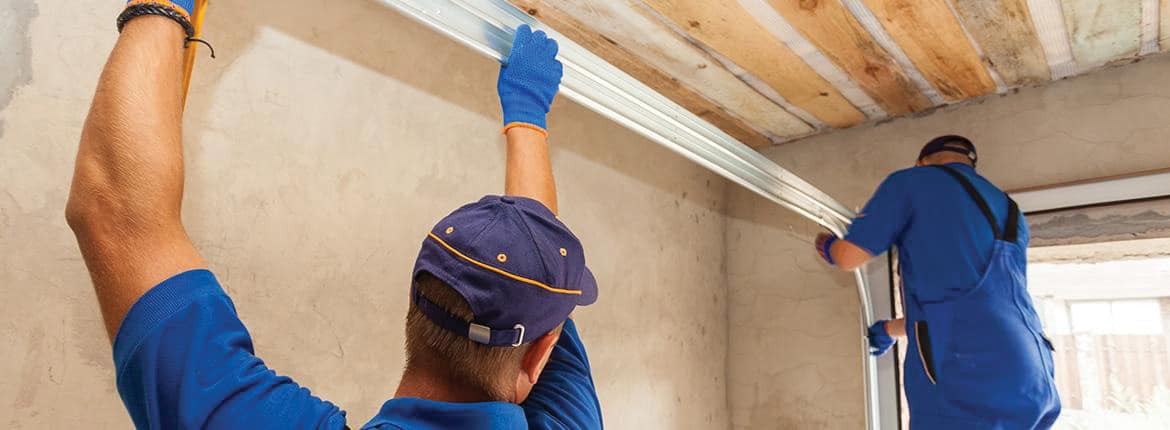 A technician installing a torsion spring on the shaft above a garage door
