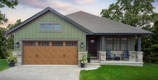 Clopay Gallery Steel garage door on green-sided house in St Thomas ON with front porch, Adirondack chairs, potted plants, gravel driveway, and landscaped yard.