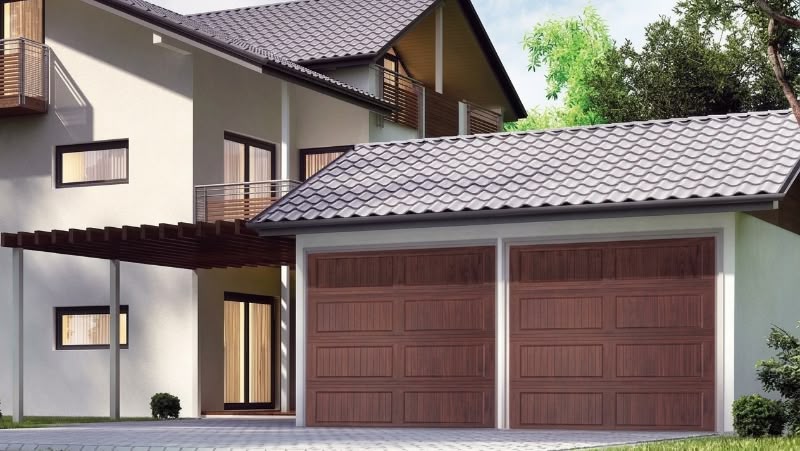 Exterior view of a modern two-story house featuring a double garage with brown wood-look carriage house doors with long grooved panels.
